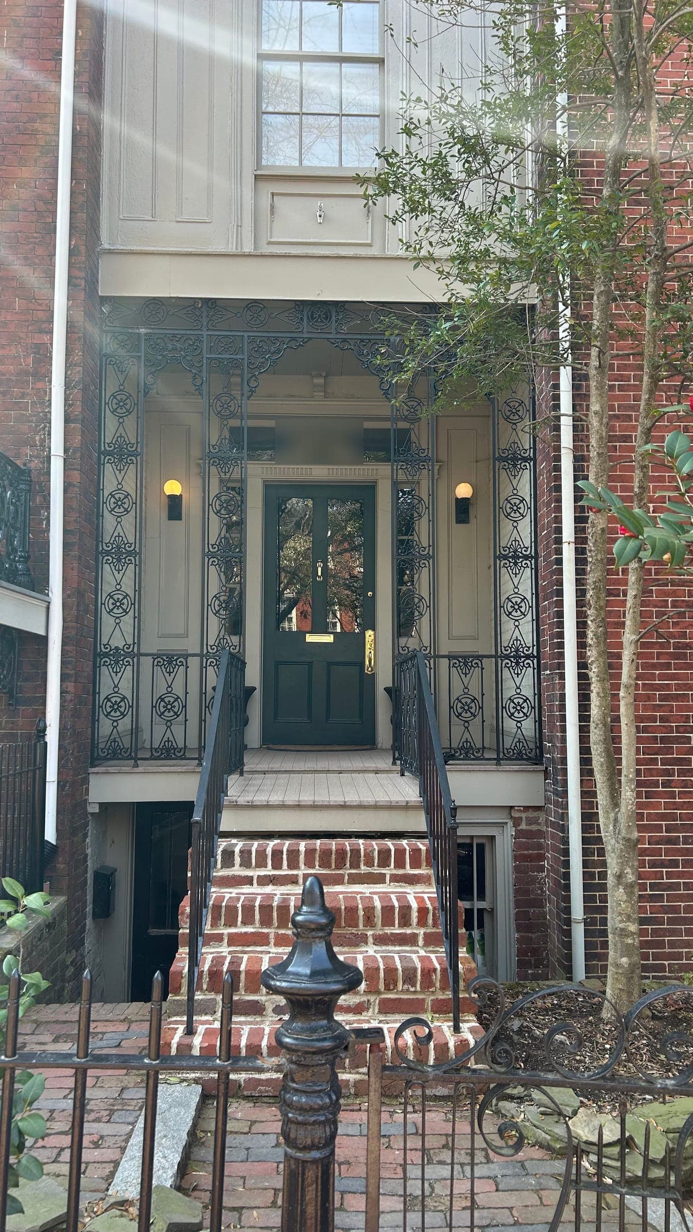 A dark green front door behind an ornamental iron porch, with brick steps leading up