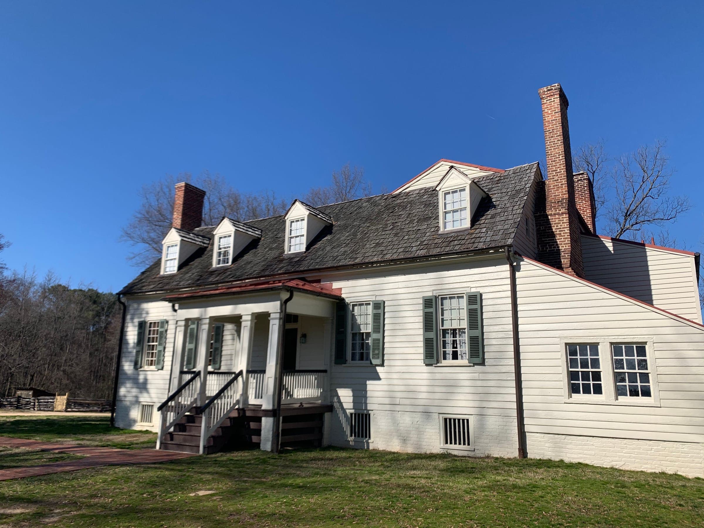 A white farmhouse with dormer windows and a front porch under a clear sky