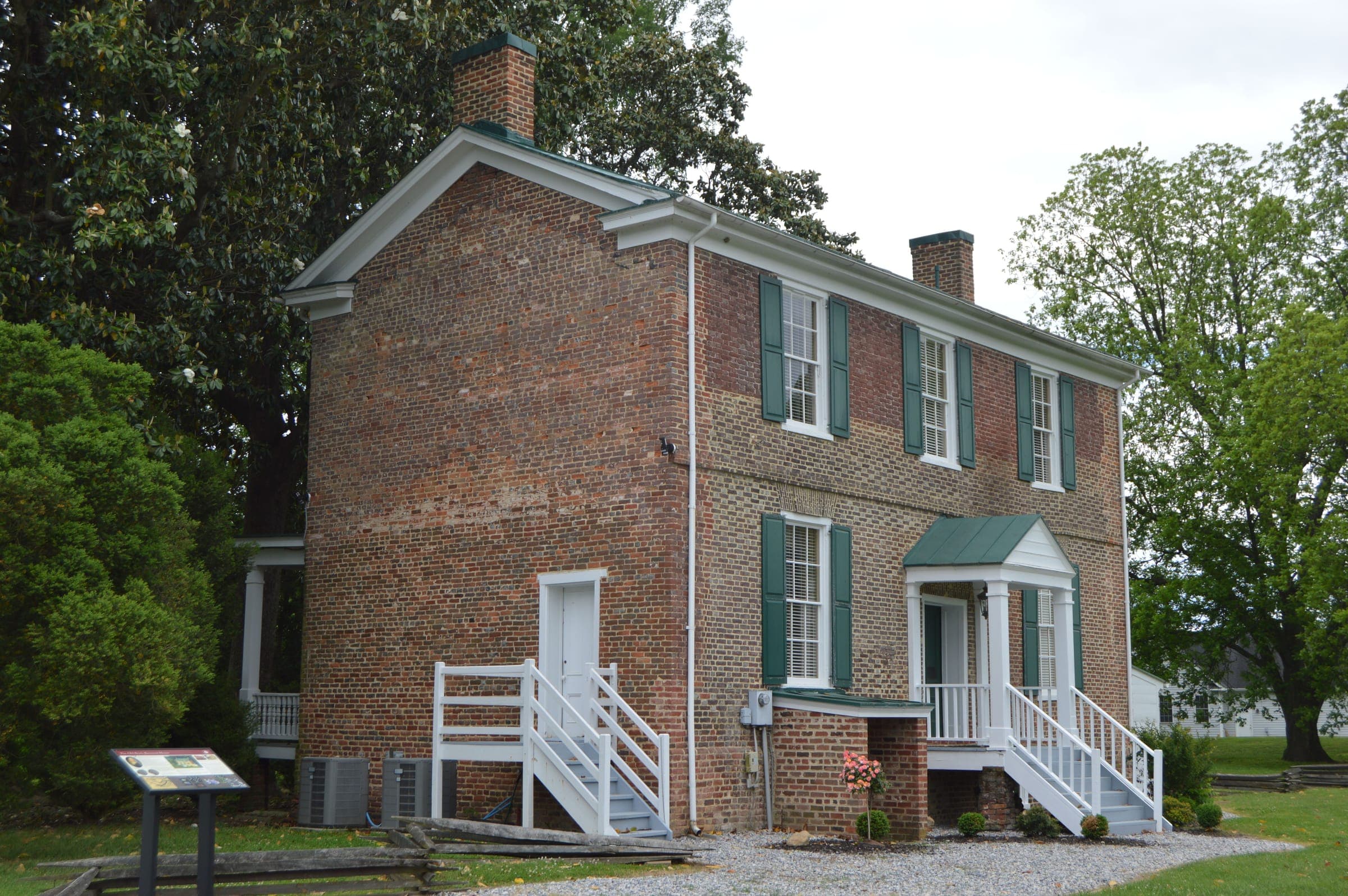 A historic two-story brick house with green shutters and white entry stairs